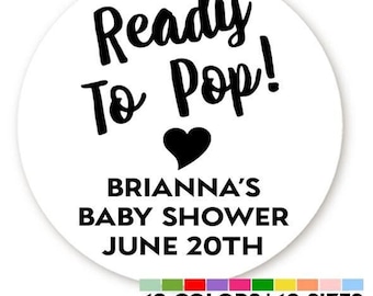 May include: Round white sticker with black text that reads "Ready To Pop!" with a black heart below the text. Below the heart is the text "Brianna's Baby Shower June 20th".