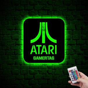 May include: Green neon sign with the Atari logo and the text "GAMERTAG" on a brick wall. The sign is illuminated with green light and has a remote control.