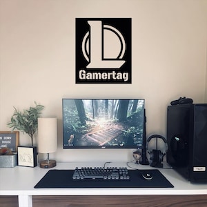 Puede incluir: Una calcoman&iacute;a de gamertag en blanco y negro con la letra L en un c&iacute;rculo, las palabras "Gamertag" debajo del c&iacute;rculo, y un monitor de computadora negro, un teclado y un mouse en un escritorio.