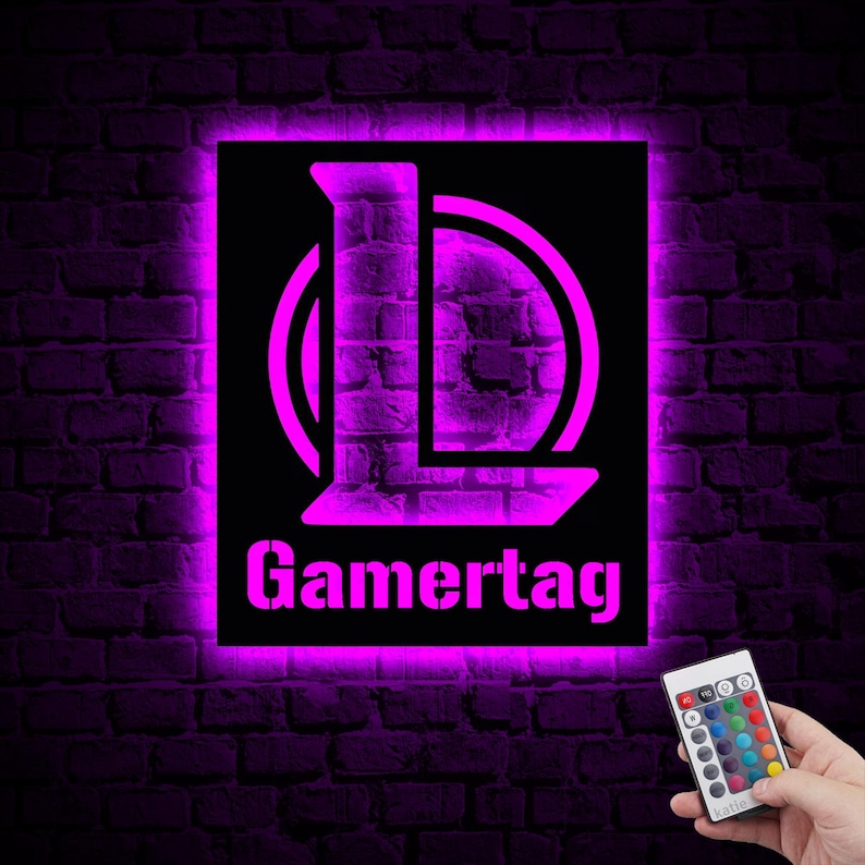 Puede incluir: Un letrero de ne&oacute;n con un brillo morado, que presenta una letra "L" estilizada dentro de un c&iacute;rculo, y el texto "Gamertag" debajo. El letrero est&aacute; montado en una pared de ladrillo e incluye un control remoto con opciones de color.