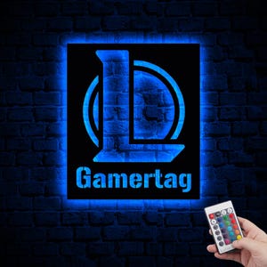 Puede incluir: Un letrero de ne&oacute;n azul con una letra L estilizada y la palabra "Gamertag" en una pared de ladrillo. El letrero est&aacute; iluminado con luz azul y tiene un control remoto para cambiar de color.