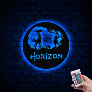 Puede incluir: Una silueta en blanco y negro de una mujer y una criatura del videojuego Horizon Zero Dawn. La silueta está en un letrero redondo, negro y luminoso con la palabra "HORIZON" en letras blancas. El letrero está en una pared de ladrillo y un mando a distancia con botones de colores está en la esquina inferior derecha de la imagen.
