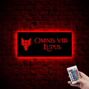May include: A red neon sign with the text "OMNIS VIR LUPUS" and a wolf head graphic. The sign is mounted on a brick wall and has a remote control for changing the color of the neon lights.