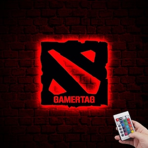 Puede incluir: Un letrero de gamertag rojo y negro con el texto "GAMERTAG" en una pared de ladrillo. El letrero está iluminado con luces LED rojas y viene con un control remoto para cambiar el color de las luces.