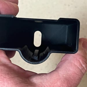 Pode incluir: Caixa de plástico preto com uma abertura retangular e um furo redondo no centro.