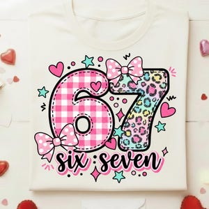 May include: Cream-colored t-shirt featuring a colorful graphic design for a sixth birthday. The number "6" is in pink gingham, and the "7" has a leopard print. The words "six: seven" are written below the numbers, with hearts, stars, and bows.