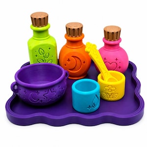 Puede incluir: Un conjunto de artículos de plástico coloridos para hacer pociones sobre una bandeja morada ondulada, que incluye un caldero morado, una botella verde lima con una hoja, una naranja con una luna, una rosa con un corazón, una taza azul y una cuchara amarilla.