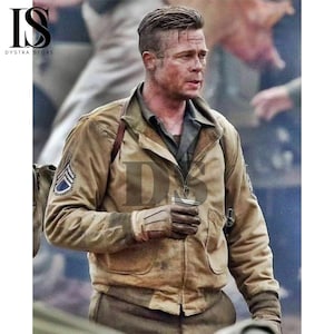 Może przedstawiać: Beżowa kurtka w stylu wojskowym z zapięciem na zamek błyskawiczny, noszona przez osobę z poważnym wyrazem twarzy. Kurtka ma naszywkę na lewym rękawie i jest noszona z rękawicami. Obraz ma estetykę vintage.