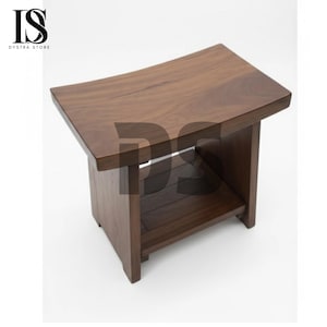 May include: A dark brown wooden stool with a rectangular top and a lower shelf. The stool has a curved top and a simple, modern design. The wood grain is visible on the surface.