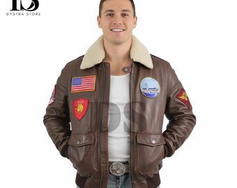 Puede incluir: Chaqueta de cuero marrón con cuello de borrego color crema. La chaqueta presenta varios parches, incluyendo una bandera americana y una escena de faro. Tiene dos bolsillos delanteros y un dobladillo y puños acanalados.
