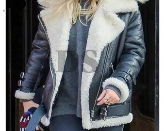 May include: Black shearling aviator jacket with a white faux fur lining and collar. The jacket features a zipper closure, buckled cuffs, and a classic aviator design. A stylish outerwear piece for cold weather.