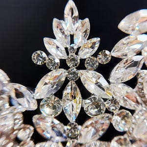 May include: Close-up of a sparkling tiara with clear, faceted crystals. The tiara features a floral design with various shapes of crystals, including marquise and round cuts. The crystals are set in a silver-toned metal, creating a glamorous look.