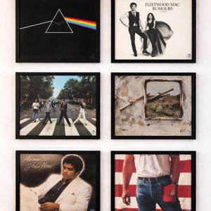 May include: Collection of framed album covers, including Pink Floyd's "Dark Side of the Moon" with a prism and rainbow, Fleetwood Mac's "Rumours", and others. The frames are black, creating a cohesive display.