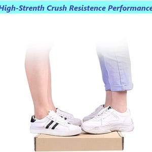 May include: Two people stand on a cardboard box, each wearing white trainers with black accents. The box is labelled "High-Strength Crush Resistance Performance".