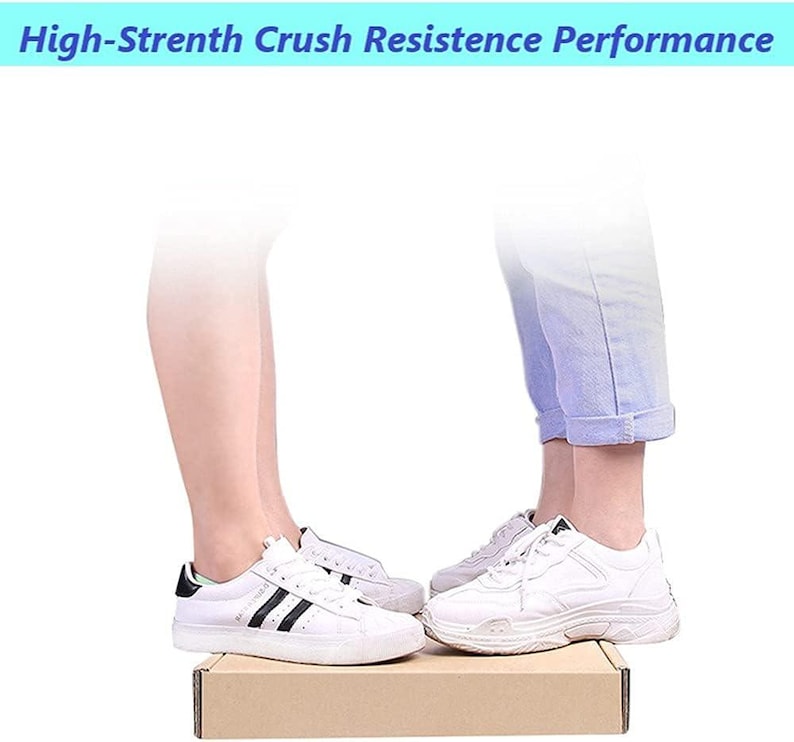 May include: Two people stand on a cardboard box, each wearing white trainers with black accents. The box is labelled "High-Strength Crush Resistance Performance".