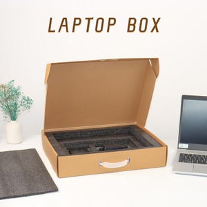 May include: A brown cardboard box with a handle, open to reveal a foam interior designed to protect a laptop. The box is labelled "LAPTOP BOX".