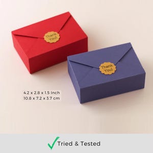 Puede incluir: Dos peque&ntilde;as cajas con forma de sobre, una roja y otra morada, con una pegatina dorada de "&iexcl;Gracias!" en cada una. Las cajas miden 4,2 x 2,8 x 1,5 pulgadas o 10,8 x 7,2 x 3,7 cent&iacute;metros.