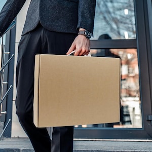May include: A person carrying a brown cardboard box with a white handle.