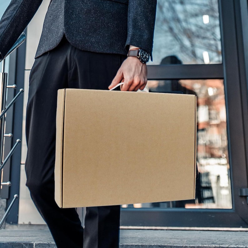 May include: A person carrying a brown cardboard box with a white handle.