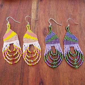 May include: A pair of beaded earrings with a geometric design. The earrings are made with small, colorful beads in shades of pink, yellow, green, and purple. The earrings are dangle style and have a silver hook.