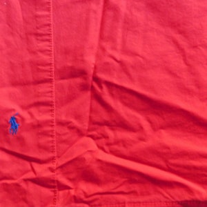 May include: Red cotton fabric with a small blue polo player logo embroidered on the left side.
