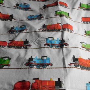 May include: A white fabric with a repeating pattern of Thomas the Tank Engine and his friends. The trains are blue, red, and green and are on a brown track. The fabric is likely a bed sheet or a duvet cover.