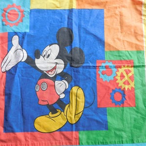 May include: A colorful sheet featuring a large image of Mickey Mouse in his classic outfit, set against a patchwork of red, blue, yellow, and green squares. The design includes gear-shaped graphics.
