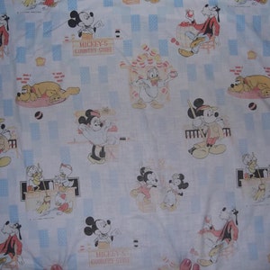 Pu&ograve; includere: Un tessuto bianco con un motivo ripetuto di personaggi Disney, tra cui Topolino, Minni, Paperino, Pippo e Pluto. La stampa include il testo Mickey's Country Store, con accenti rettangolari azzurri distribuiti su tutto il design.