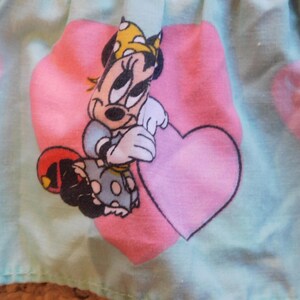 Puede incluir: Una tela azul claro con un coraz&oacute;n rosa y una imagen de dibujos animados de Minnie Mouse sosteniendo un coraz&oacute;n rosa. Minnie Mouse lleva un vestido de lunares rojos y blancos y un lazo amarillo.