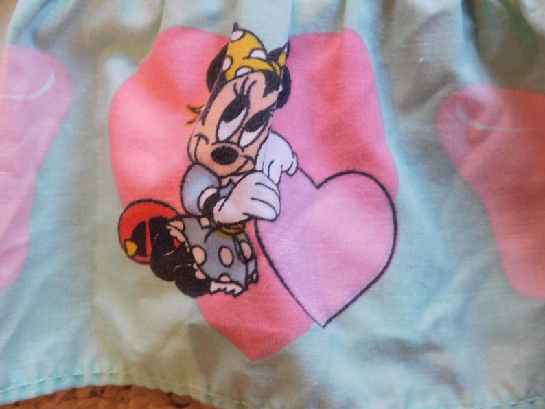 Puede incluir: Una tela azul claro con un coraz&oacute;n rosa y una imagen de dibujos animados de Minnie Mouse sosteniendo un coraz&oacute;n rosa. Minnie Mouse lleva un vestido de lunares rojos y blancos y un lazo amarillo.