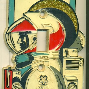 May include: A white plastic light switch cover with a colorful image of an astronaut wearing a helmet and a spacesuit. The astronaut is holding a device with a red and white striped flag. The switch cover has the text "Epcot Center Future World" printed on it.