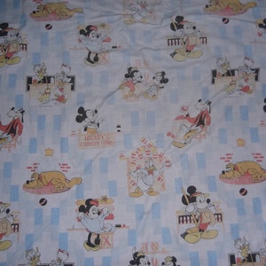 Pu&ograve; includere: Un tessuto bianco con un motivo ripetuto di personaggi Disney, tra cui Topolino, Minnie, Paperino e Pluto. La stampa presenta scene del Mickey's Country Store con accenti rettangolari blu e vari piccoli oggetti.