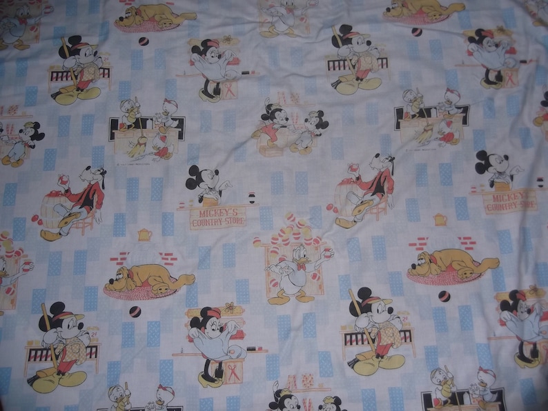 Pu&ograve; includere: Un tessuto bianco con un motivo ripetuto di personaggi Disney, tra cui Topolino, Minnie, Paperino e Pluto. La stampa presenta scene del Mickey's Country Store con accenti rettangolari blu e vari piccoli oggetti.