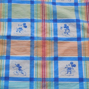 May include: A blue and white checkered fabric with a repeated pattern of Mickey Mouse in blue. The fabric has red, orange, and green stripes.