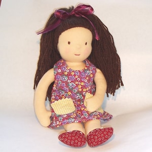 May include: A handmade doll with brown yarn hair, a red and white floral dress, and yellow gingham pockets. The doll is wearing red and white patterned shoes.