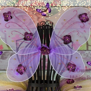 May include: Purple fairy wings with glitter and purple flowers. The wings are made of tulle and have a wire frame.