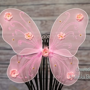 May include: Pink fairy wings with gold glitter and pink flowers. Created by Malishka Boutique.