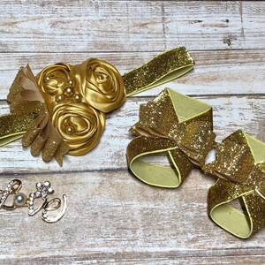 Op de afbeelding: Een set van twee gouden glitter haarbandjes met elastiekjes. De strikken zijn in de vorm van een bloem en een strik. Er is ook een gouden bedel met het woord "Love" en een parel in het midden.