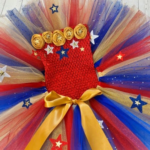 May include: Red, white, and blue tulle tutu with gold glitter and a red crocheted top with gold and white star embellishments.