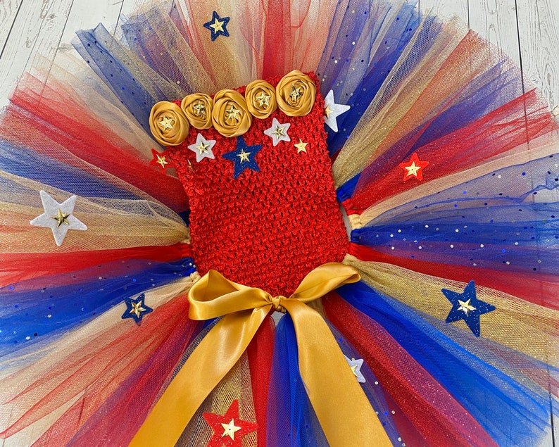 May include: Red, white, and blue tulle tutu with gold glitter and a red crocheted top with gold and white star embellishments.