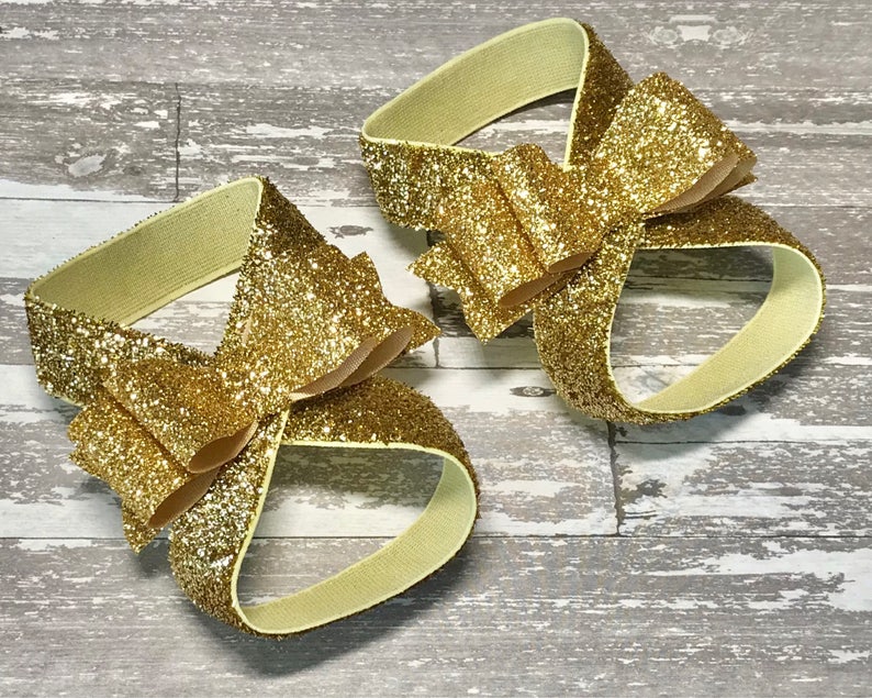 Op de afbeelding: Een paar gouden glitter enkelbandjes met een grote gouden glitter strik op elk bandje.
