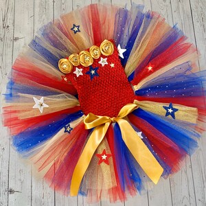 May include: Red, white, and blue tulle tutu with gold ribbon and gold stars. The tutu has a red crocheted top with gold flowers and white stars.