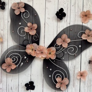 May include: Black and silver fairy wings with a delicate design and blush pink flower accents.