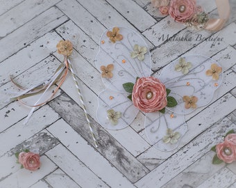 May include: White butterfly fairy wings with a pink flower and green leaves. The wings are decorated with glitter and small orange beads. A matching wand with a pink flower and green leaves is also included. Created by Malishka Boutique.