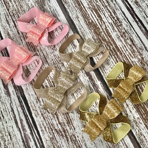 Op de afbeelding: Vier paar glimmende stoffen strikjes voor in het haar. Twee paar zijn roze en twee paar zijn goud.