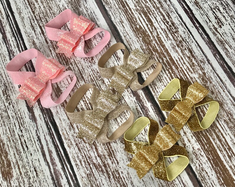 Op de afbeelding: Vier paar glimmende stoffen strikjes voor in het haar. Twee paar zijn roze en twee paar zijn goud.
