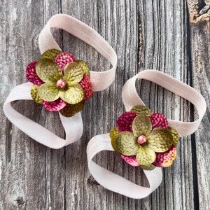 Puede incluir: Dos cintas para el pelo de tela con flores rosas y verdes y una cuenta rosa en el centro de cada flor.