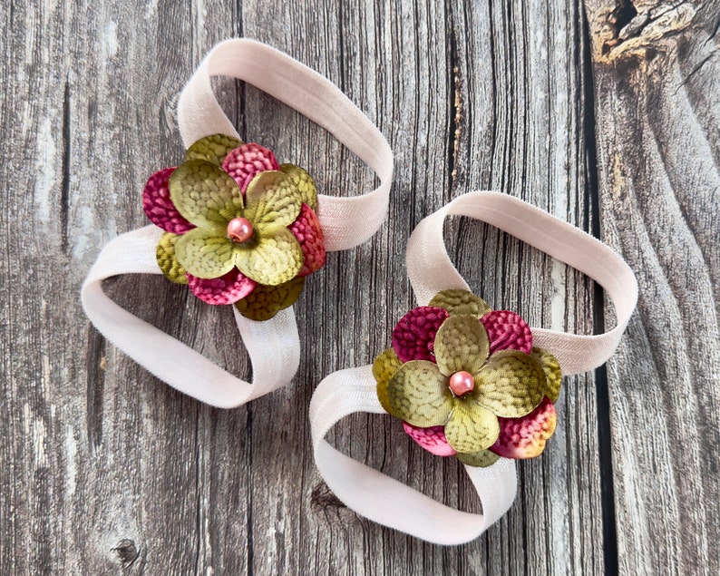 Puede incluir: Dos cintas para el pelo de tela con flores rosas y verdes y una cuenta rosa en el centro de cada flor.