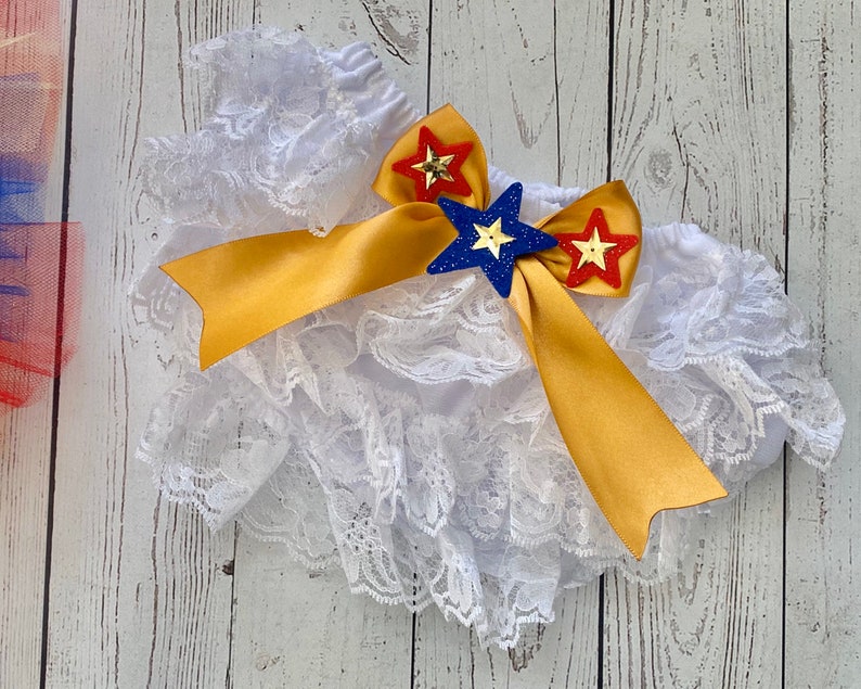May include: White lace ruffle bloomers with a gold satin bow and red, blue, and yellow star embellishments.