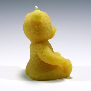 May include: A yellow, bear-shaped candle with a white wick. The candle is sculpted in a sitting position, with its arms gently curved. The bear has a textured surface, giving it a soft appearance. This decorative candle is suitable for home decor.